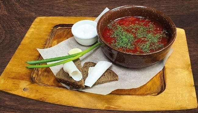 Борщ боярский в фарфоровой тарелке с ложкой сметаны и зеленью