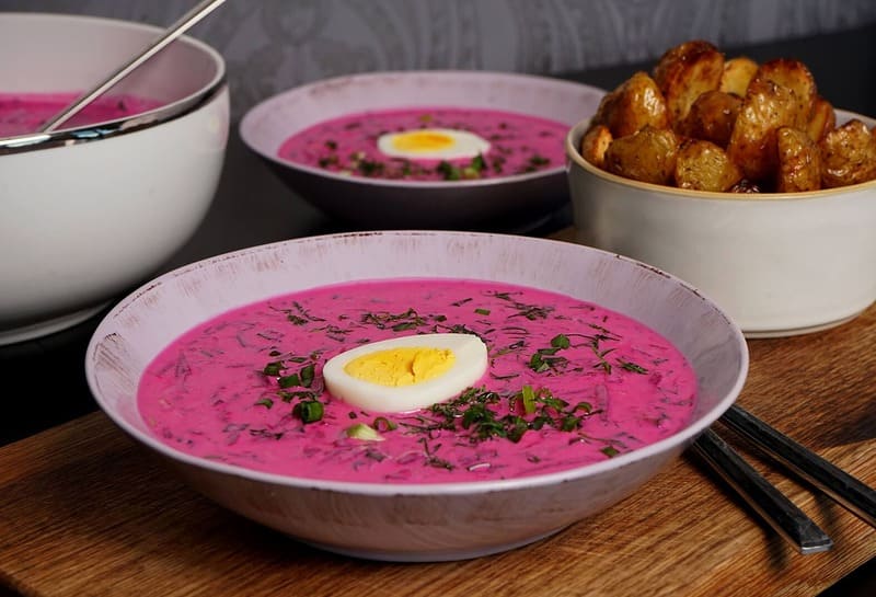 Холодный литовский борщ на кефире: ярко-розовый суп в тарелке с кусочками свеклы, огурца и яйца, рядом горячий картофель в мундире