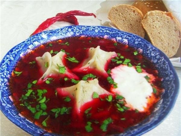 Польский борщ с ушками Польский борщ: наваристый красный суп в тарелке с пельменями «ушками», сметаной и зеленью